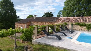 A stone building with a tiled roof, a swimming pool, and lounge chairs.