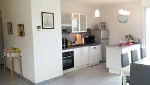 A modern kitchen with white cabinets, a dishwasher, a microwave, and a sink. There is a small wooden table with toys on it.