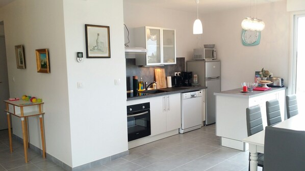A modern kitchen with white cabinets, a dishwasher, a microwave, and a sink. There is a small wooden table with toys on it.