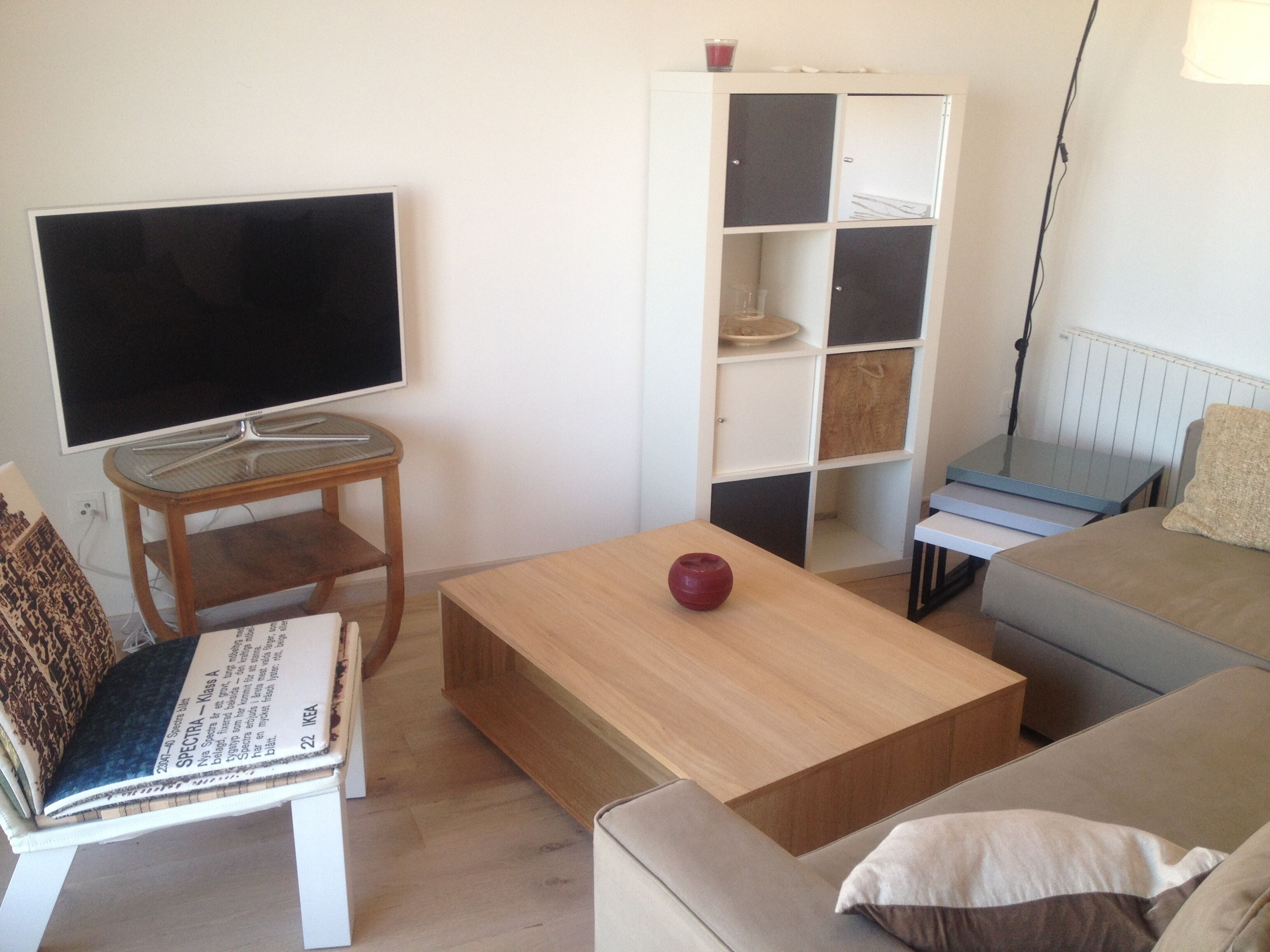 A living room with a flat-screen TV, a wooden coffee table, a sofa, a bookshelf, and a lamp.