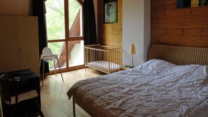 Ein Zimmer mit einem Bett, einem Kinderbettchen, einem Schreibtisch und einem Fenster mit Vorhängen.