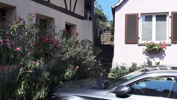 Une voiture est garée devant un immeuble, et un escalier mène à une porte.