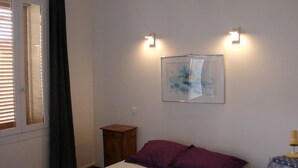 A bedroom with a bed, a small wooden nightstand, a wall-mounted abstract painting, and two wall-mounted lights. - TYPICAL HOUSE IN THE HEART OF THE VILLAGE, ENTIRELY RENOVATED, 200M FROM THE BEACH (Le Barcarès)
