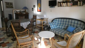 A living room with a checkered sofa, wicker chairs, a dining table with chairs, a TV mounted on the wall, and a bookshelf. - TYPICAL HOUSE IN THE HEART OF THE VILLAGE, ENTIRELY RENOVATED, 200M FROM THE BEACH (Le Barcarès)