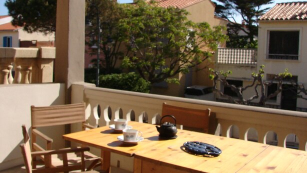 A wooden table with chairs, a teapot, and cups, set against a backdrop of buildings and trees. - TYPICAL HOUSE IN THE HEART OF THE VILLAGE, ENTIRELY RENOVATED, 200M FROM THE BEACH (Le Barcarès)