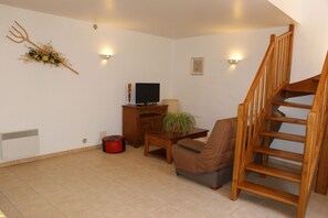 Ein Wohnzimmer mit einer Couch, einem Couchtisch, einem Fernseher, einer Pflanze und einer Holztreppe.