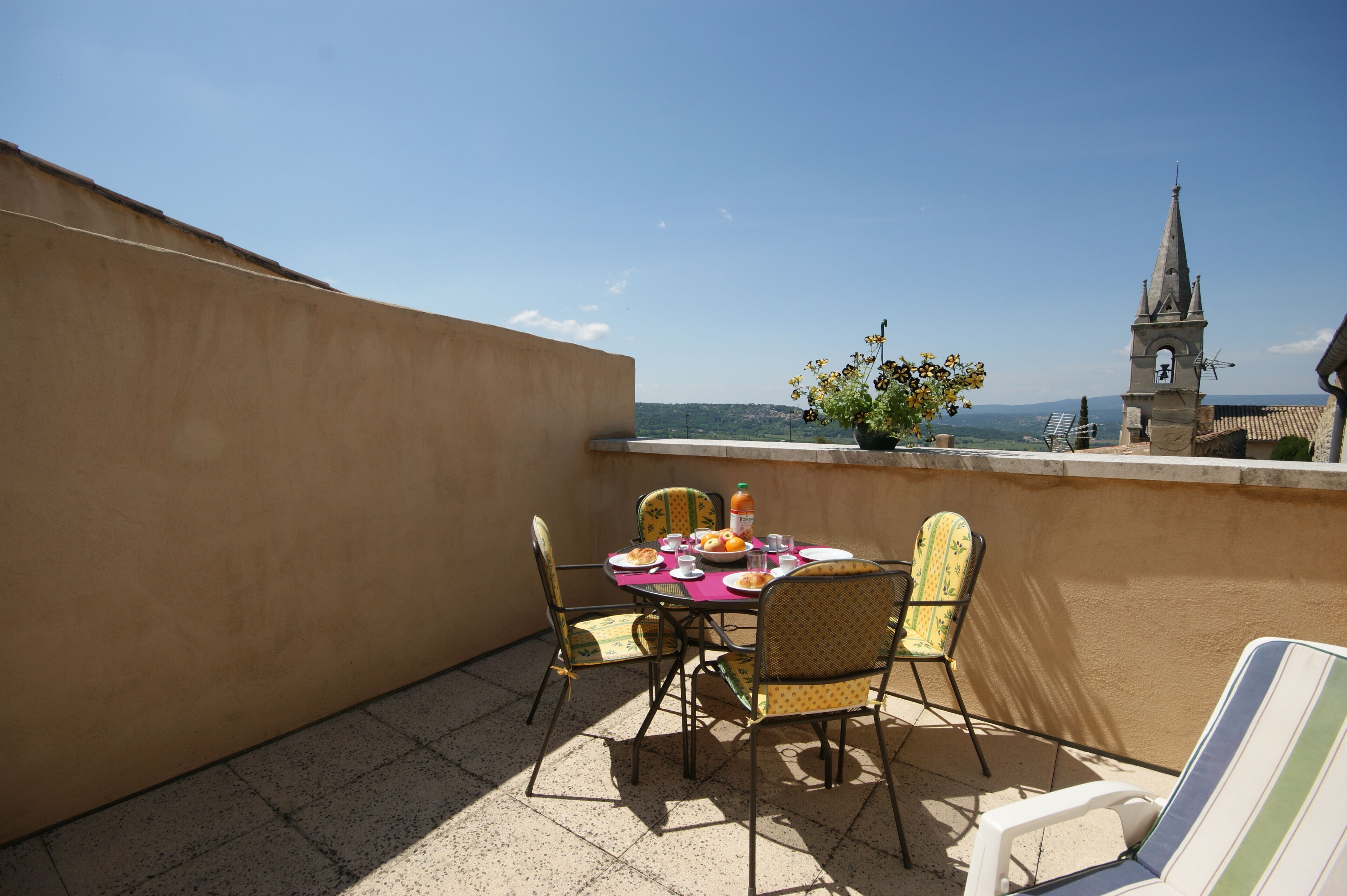 A terrace with a table set for two, chairs, and a view of a church tower.
