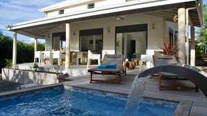 Ein modernes Haus mit Pool, Sitzgelegenheiten im Freien und einer überdachten Terrasse.
