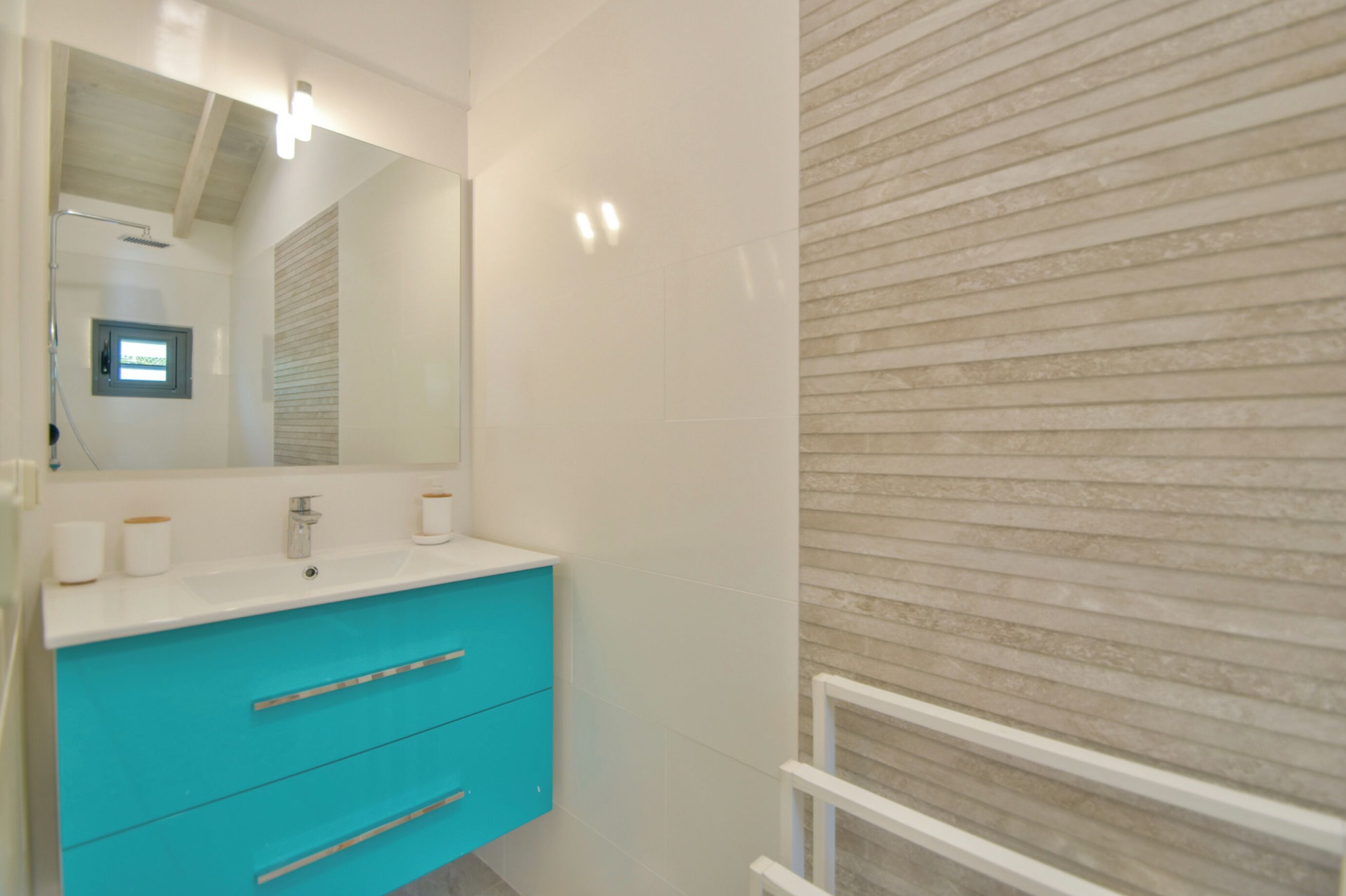 Casa de banho com lavatório branco, armário turquesa e espelho.