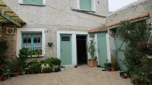 A stone building with a courtyard, featuring a central door, two windows with shutters, and potted plants around the area. - independent house in property retaise for 4 people (Le bois plage)