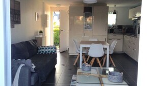 Um espaço compacto com sofá, mesa de jantar com cadeiras, cozinha e porta de vidro que dá para o exterior.
