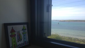 Ein gerahmtes Bild mit bunten Gebäuden an einer Wand, ein Fenster mit Blick auf ruhiges Wasser und entferntes Land.