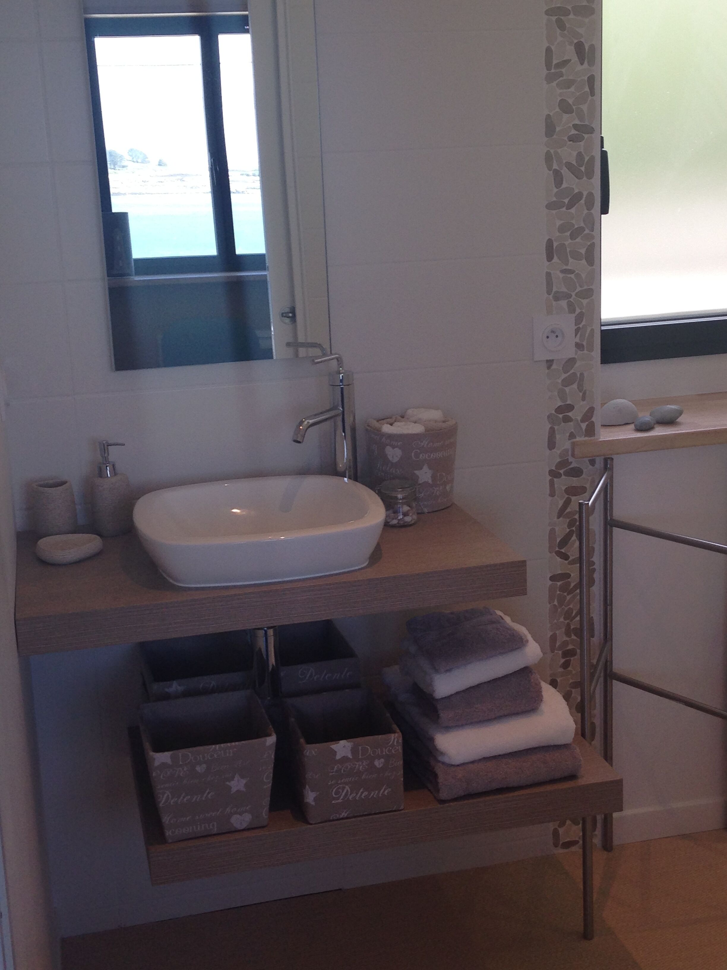 A bathroom with a white sink, a mirror, a towel rack, and storage boxes.