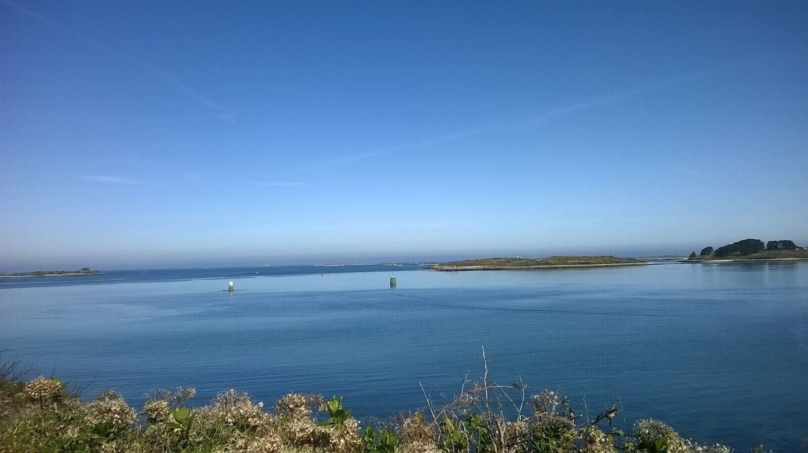 Un paisaje costero con un mar tranquilo, una pequeña isla y una costa distante.