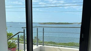 Ein Balkon mit Holzdeck, Metallgeländer und Blick auf das Meer und das entfernte Land.