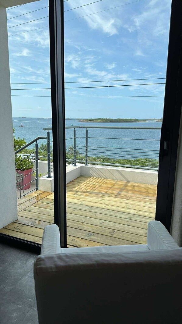 A balcony with a wooden deck, a metal railing, and a view of the sea and distant land.