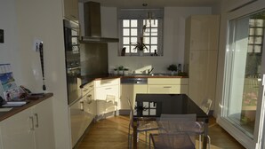 Eine moderne Küche mit Holzboden, einem Esstisch mit Stühlen und einem Fenster mit Jalousien.