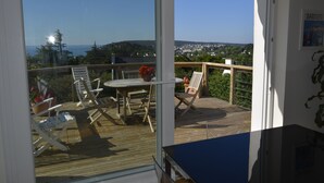 Ein Balkon mit Tisch und Stühlen, Blick aufs Meer und eine Stadtkulisse im Hintergrund.