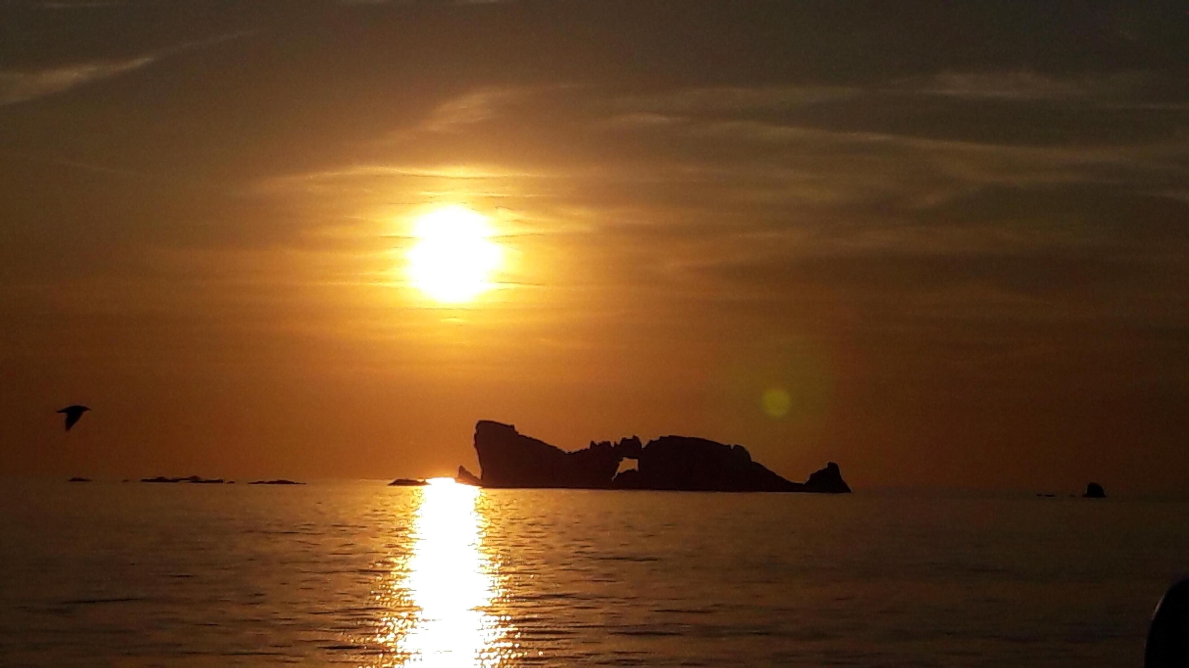 Un capvespre sobre un mar tranquil amb la silueta d'una formació rocosa.