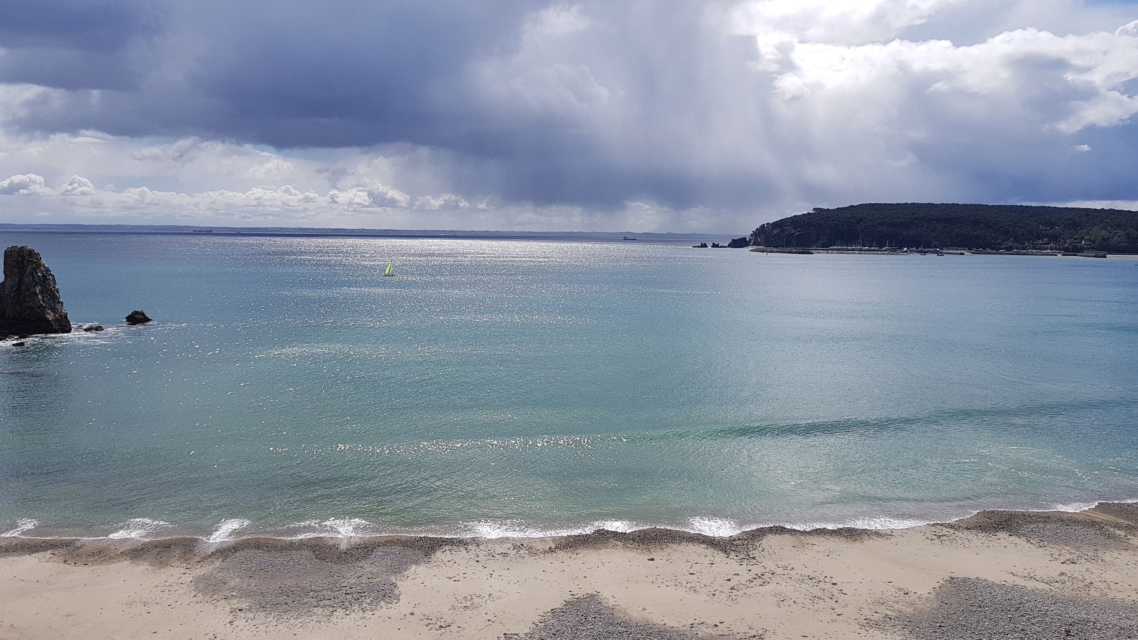 Una playa con agua cristalina, un promontorio rocoso y una isla distante.