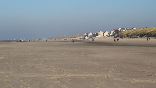 A wide sandy beach with people walking and a row of houses on the hillside. - Sea view at Fort Mahon Plage in the Somme studio 4 people (Fort-Mahon-Plage)