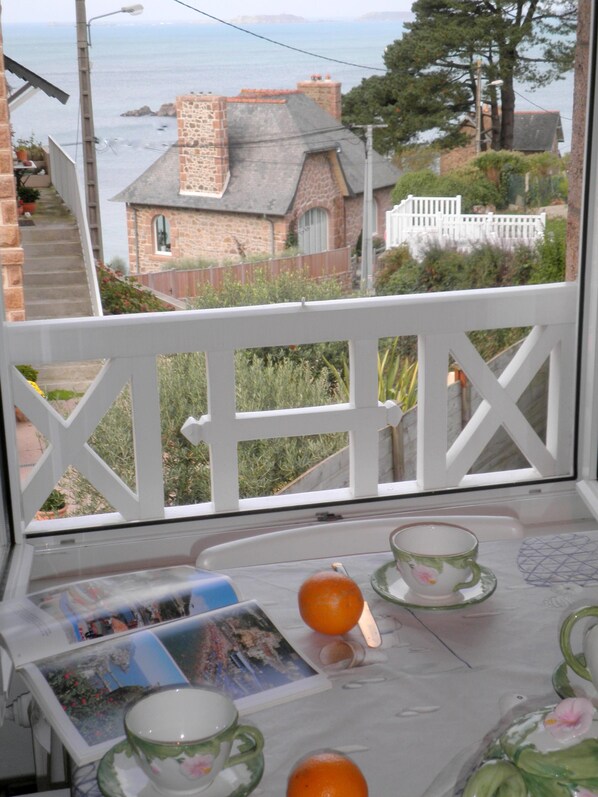 Un balcone con vista sulla costa, che include un tavolo con una tazza, un piattino, un'arancia e una cartolina.