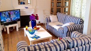 A living room with a TV, a sofa, a coffee table with a bowl of fruit, and a vase with flowers. - Villa 3 bedrooms / Walking distance / Sea view / Beach 200 m (Perros-Guirec)