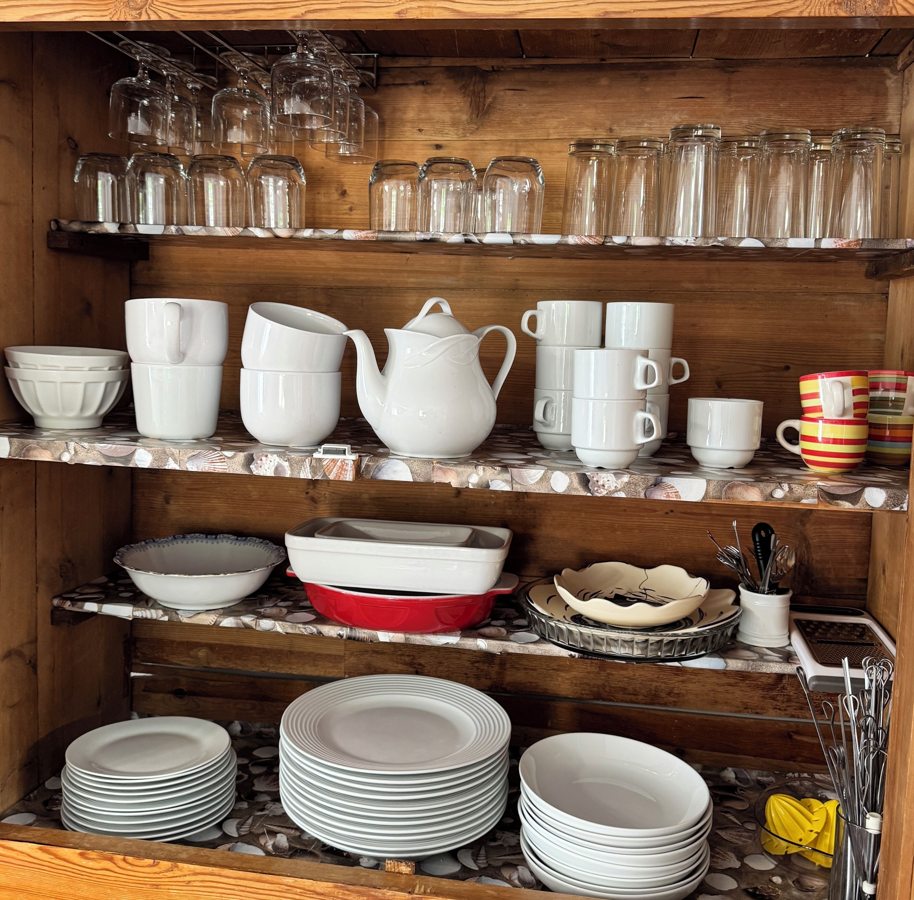 Un estante de madera con distintos utensilios de cocina, como tazas, cuencos y platos.