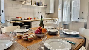 A well-lit kitchen with white cabinets, a stainless steel range hood, and a built-in dishwasher. There is a dining table set with plates, glasses, and a bottle of wine. - Villa 3 bedrooms / Walking distance / Sea view / Beach 200 m (Perros-Guirec)
