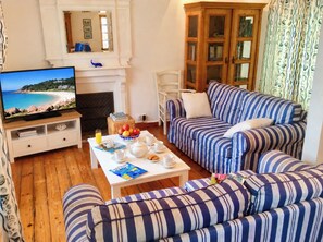 Ein Wohnzimmer mit Fernseher, Kamin, einer gestreiften Sofagarnitur und einem Esstisch mit Frühstücksangebot.