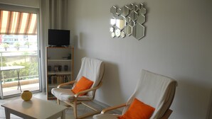 A living room with two white armchairs, a small table, a bookshelf, and a TV. - Bright 52m2 air-conditioned apartment with Wifi and single-storey closed garage (Fréjus)