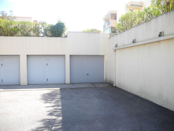 A parking area with three closed garage doors, a concrete wall, and a clear sky.