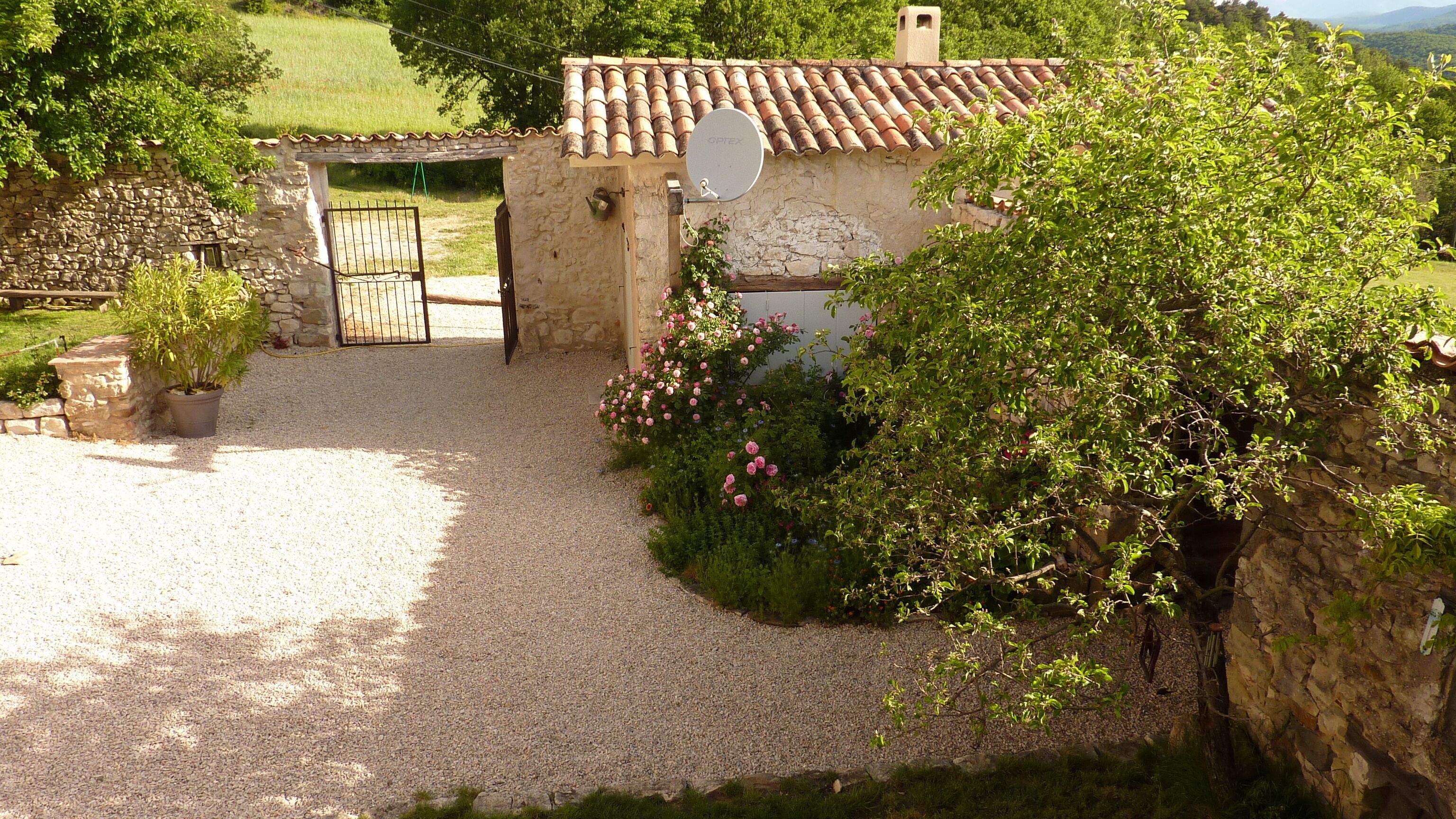 Un bâtiment rustique en pierre, avec une allée de gravier menant à une entrée fermée par un portail.
