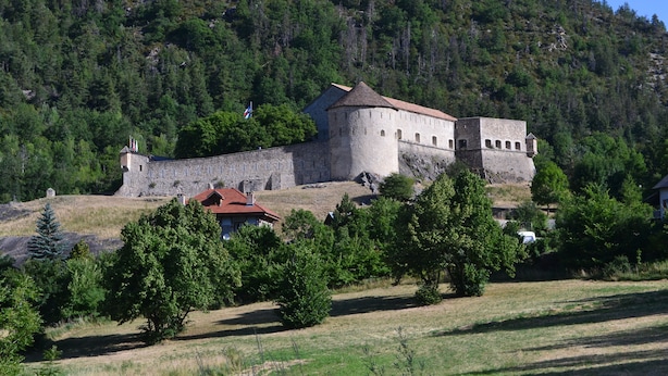 A historic stone castle with a fortified wall and a red-roofed building in the foreground. - Spacious apartment in chalet with a beautiful view! (Allos)