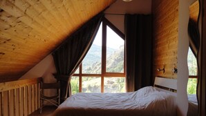 A bedroom with a wooden ceiling, a large window with curtains, a bed, and a chair. - Spacious apartment in chalet with a beautiful view! (Allos)