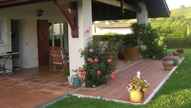 Un patio couvert avec un sol carrelé, une chaise en bois, une table et des plantes en pot.