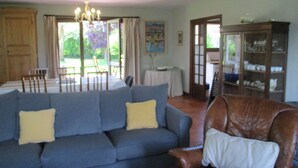 Un salon avec un canapé bleu, un fauteuil en cuir marron et un coin repas comprenant une table et des chaises.