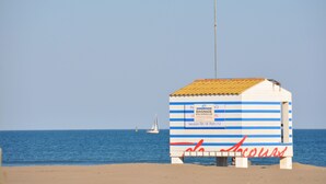 A beach hut with a striped exterior, a sign indicating it is a non-surveilled area, and a sailboat in the background. - MAGNIFICENT, COMFORTABLE TRADITIONAL CHALET FACING THE SEA (Gruissan)
