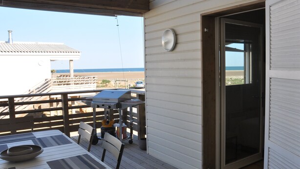 A covered outdoor area with a table and chairs, a grill, and a view of the beach. - MAGNIFICENT, COMFORTABLE TRADITIONAL CHALET FACING THE SEA (Gruissan)