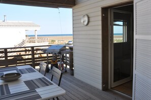 Un espace extérieur abrité, équipé d’une table et de chaises, d’un barbecue et offrant une vue sur la plage.