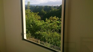 A window with a view of a lush green landscape and distant mountains. - 3 room apt. for 2-6 people, sea view, pool, air conditioning; Guadeloupe centre (Le Gosier)