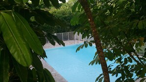 A swimming pool with a stone border, surrounded by a white fence and lush greenery. - 3 room apt. for 2-6 people, sea view, pool, air conditioning; Guadeloupe centre (Le Gosier)