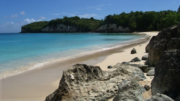 A beach with clear turquoise water, a sandy shore, and large rocks in the foreground. - 3 room apt. for 2-6 people, sea view, pool, air conditioning; Guadeloupe centre (Le Gosier)