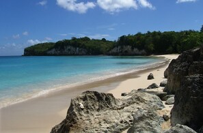 A beach with clear turquoise water, sandy shore, and large rocks. - 3 room apt. for 2-6 people, sea view, pool, air conditioning; Guadeloupe centre (Le Gosier)