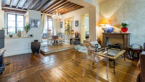 Un salon spacieux doté de parquets en bois, d’un lustre et d’une cheminée.