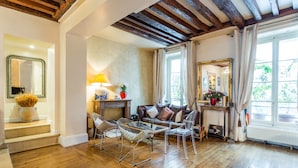 Un salon spacieux doté d’un plancher en bois, d’une cheminée et d’une grande fenêtre agrémentée de rideaux.