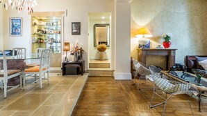 Un vaste espace de vie doté d’un plancher en bois, d’une table basse en verre et d’un fauteuil moderne. Un escalier mène à un niveau supérieur, et un coin repas comprend une table et des chaises.