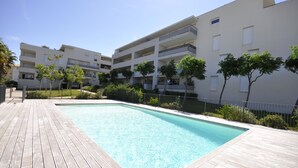 Una piscina con cubierta de madera, rodeada de edificios modernos con balcones y árboles.