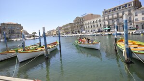 Un puerto deportivo con varias embarcaciones amarradas, un hotel destacado y un cielo azul despejado.
