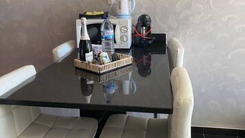 Uma mesa de jantar com uma garrafa de água, uma máquina de café e uma cesta de petiscos.